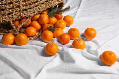 Photo of Stylish wicker bag with ripe tangerines on white bedsheet