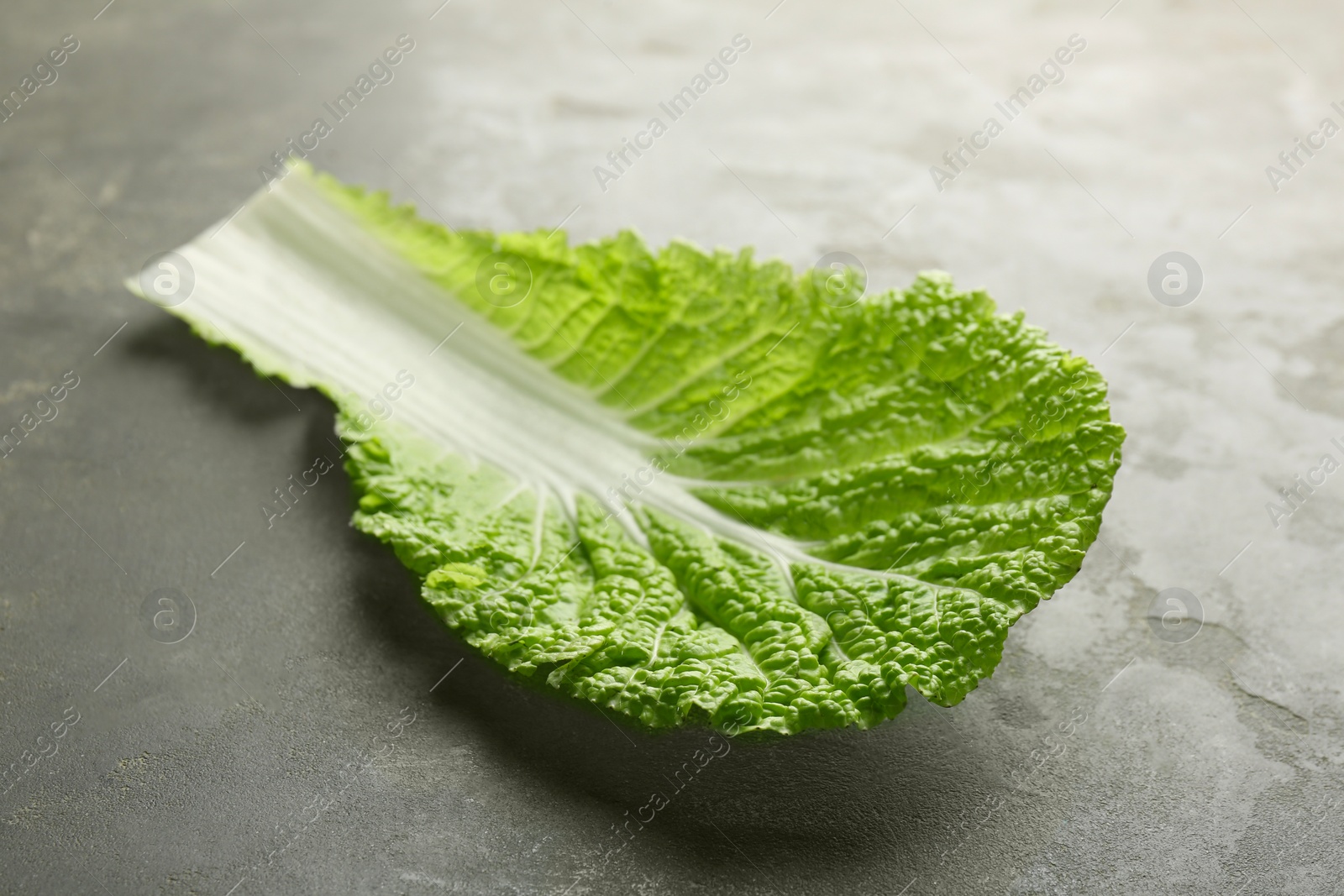 Photo of Fresh Chinese cabbage leaf on gray textured table, closeup