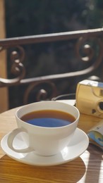 Cup of aromatic coffee and camera on wooden table outdoors