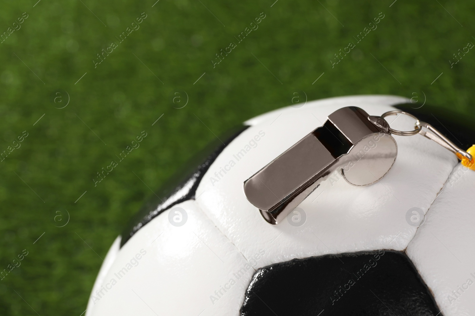 Photo of Football referee equipment. Soccer ball and metal whistle on green grass, closeup with space for text