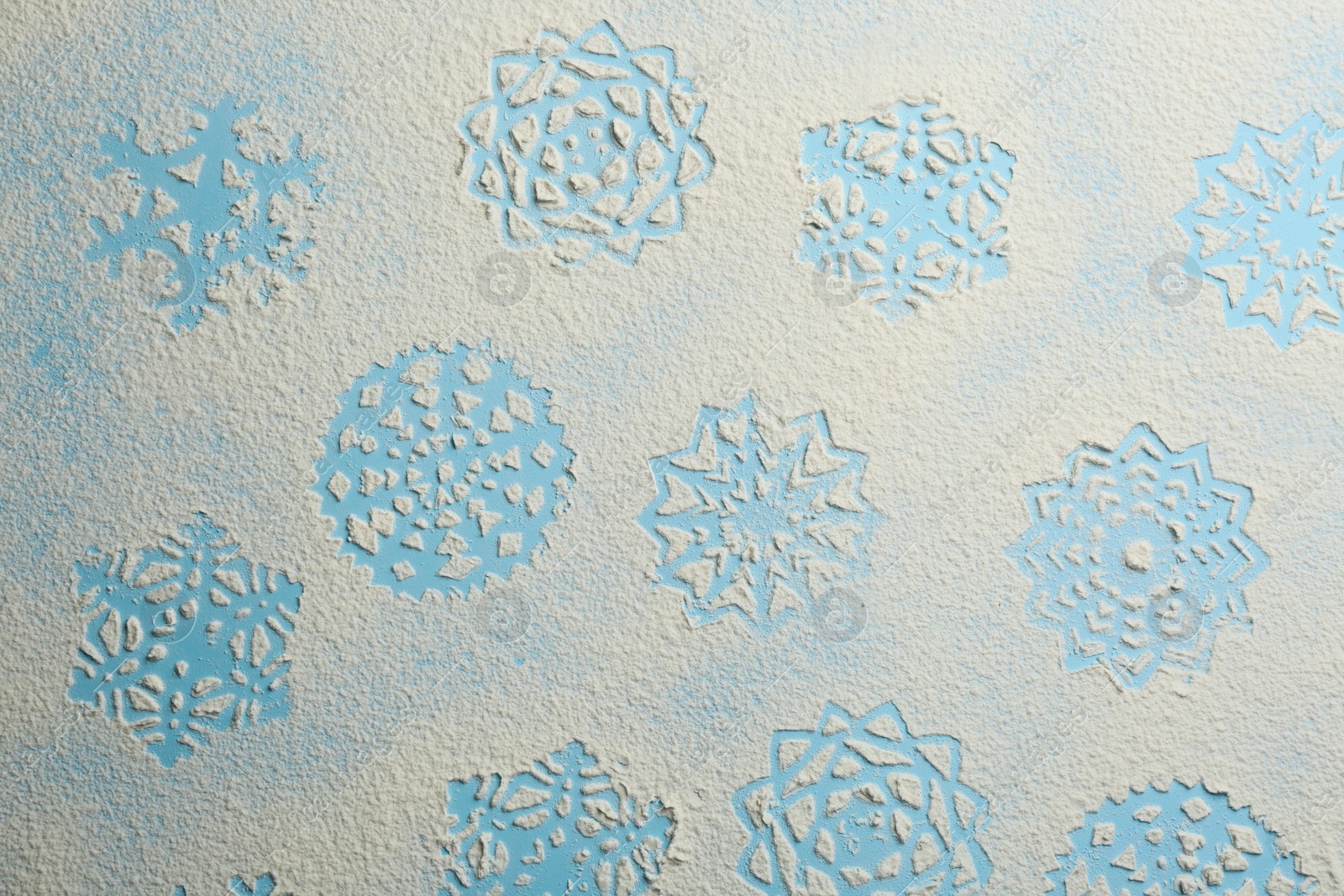 Photo of Snowflakes made of flour on light blue background, top view