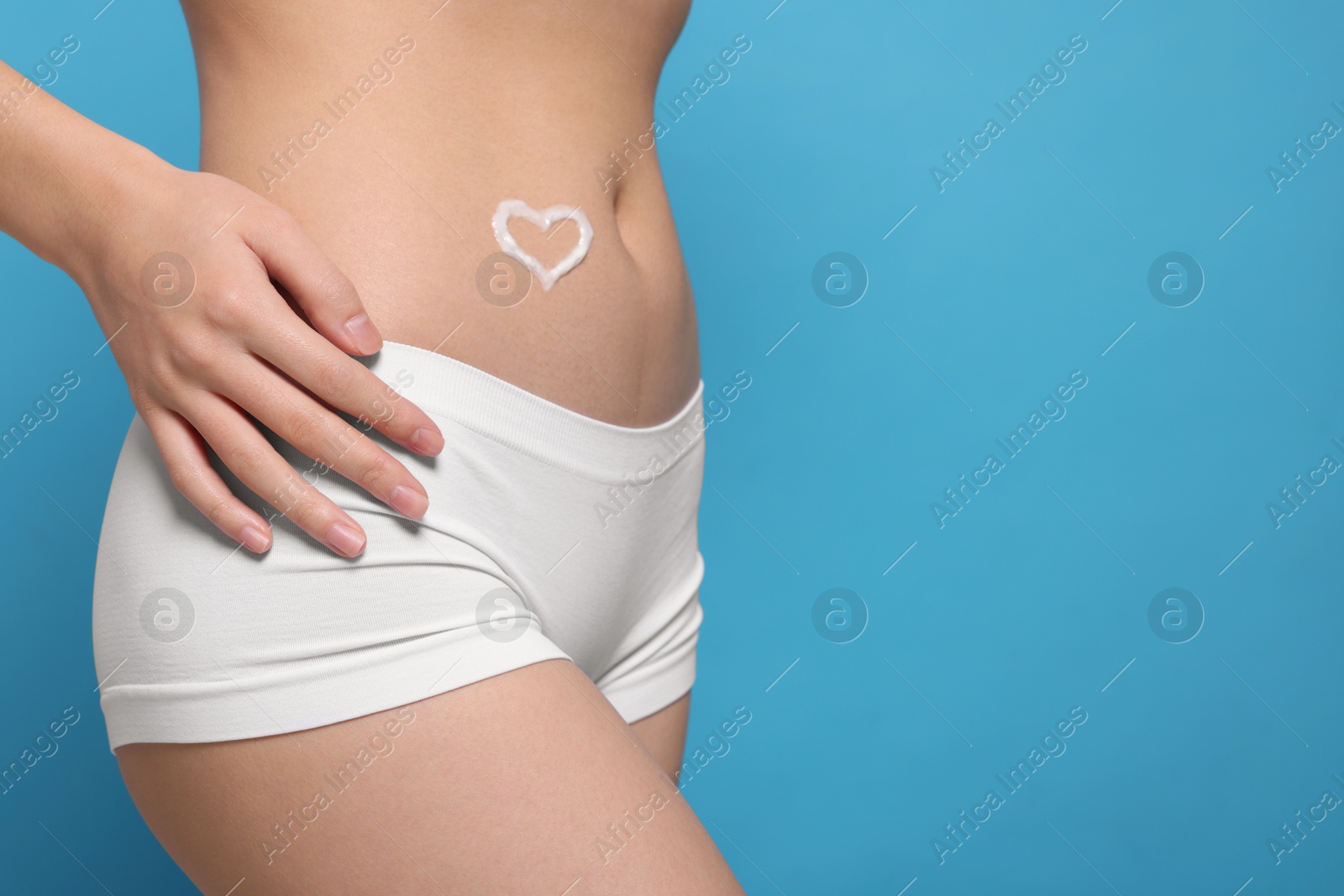 Photo of Woman with heart made of body cream on her belly against light blue background, closeup. Space for text