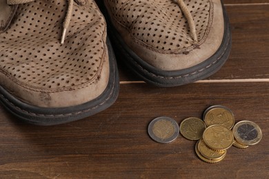 Photo of Poverty. Old shoes and coins on wooden table, closeup