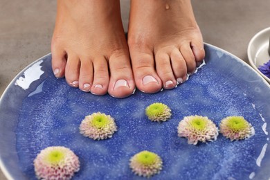 Photo of Woman soaking her feet in plate with water and flowers, closeup. Pedicure procedure