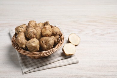 Photo of Wicker basket with many Jerusalem artichokes on white wooden table, space for text