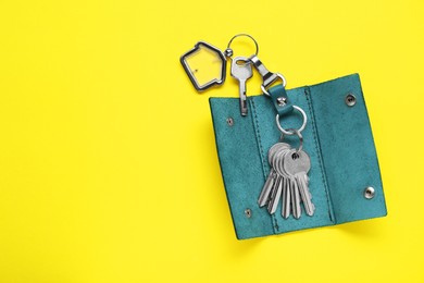 Photo of Open leather holder with keys on yellow background, top view. Space for text