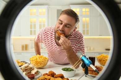 Photo of Food blogger eating near microphone at table in kitchen, view through ring light. Mukbang vlog