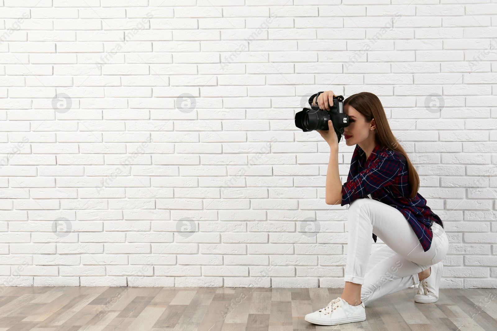 Photo of Professional photographer taking picture near white brick wall. Space for text