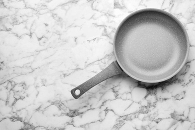 Photo of New non-stick frying pan on white marble table, top view. Space for text