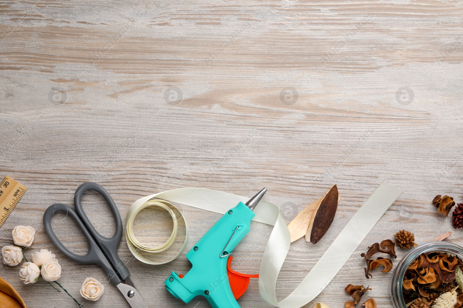 Photo of Hot glue gun and handicraft materials on white wooden table, flat lay. Space for text