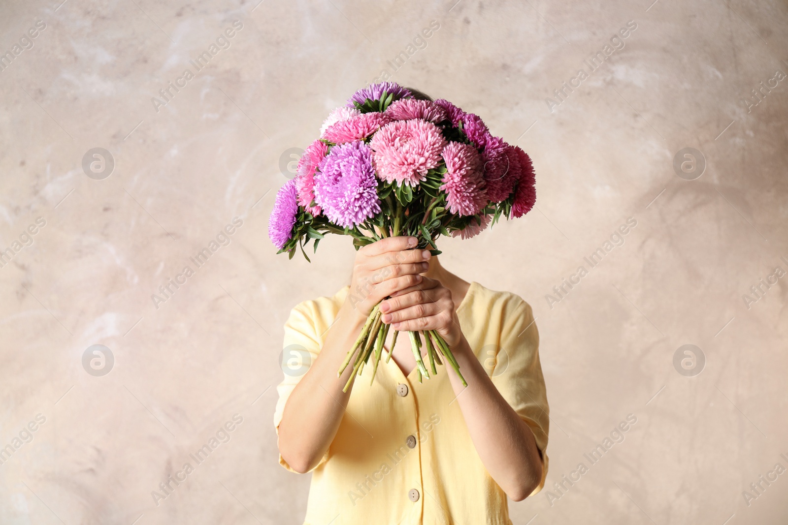 Photo of Woman holding bouquet of beautiful aster flowers on beige background