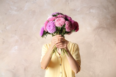 Woman holding bouquet of beautiful aster flowers on beige background