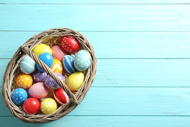 Photo of Wicker basket with painted Easter eggs on wooden background, top view. Space for text