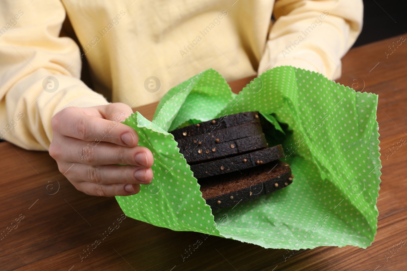 Photo of Woman packing slices of rye bread into beeswax food wrap at wooden table, closeup