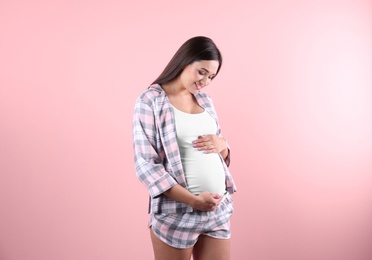 Beautiful pregnant woman holding hands on belly against color background