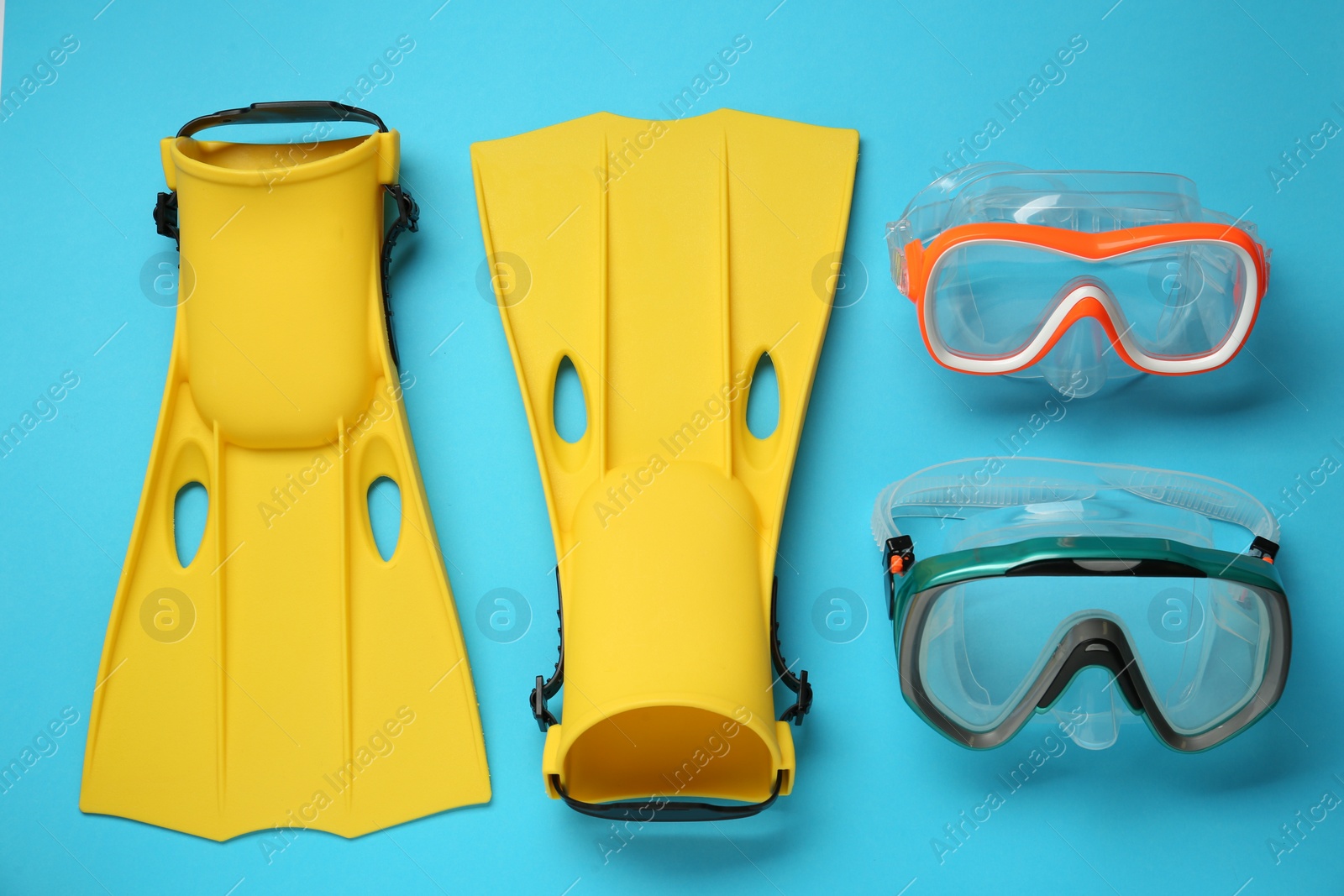 Photo of Pair of yellow flippers and masks on light blue background, flat lay