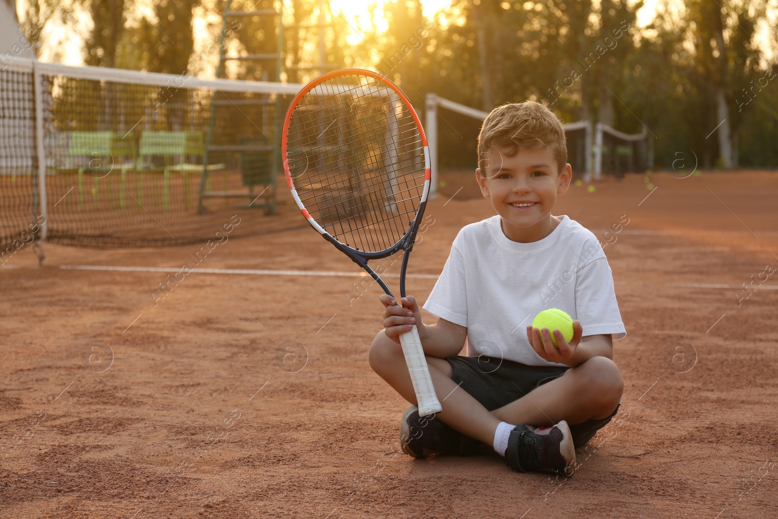 Photo of Cute little boy with tennis racket and ball on court outdoors
