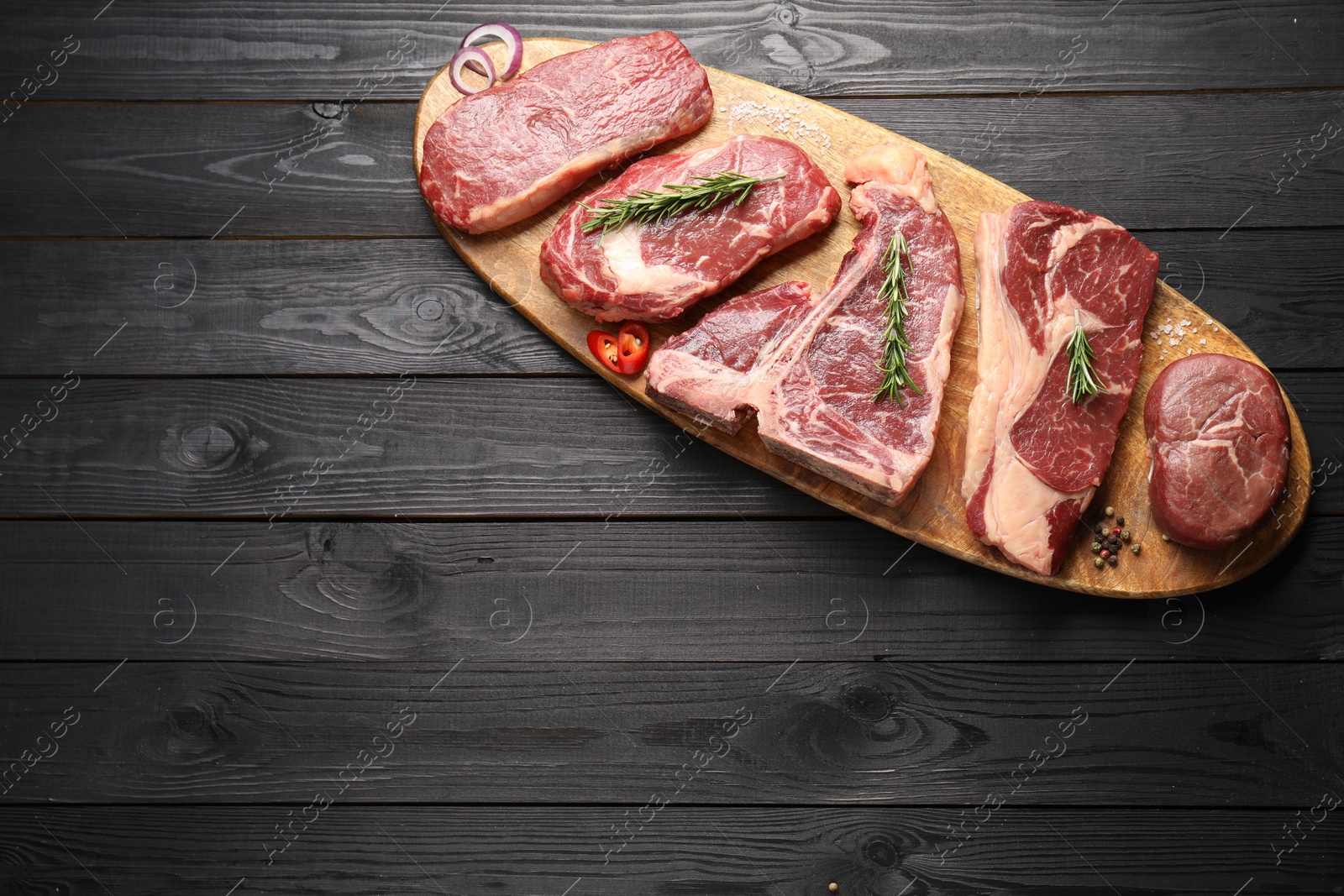 Photo of Pieces of raw beef meat and spices on black wooden table, top view. Space for text