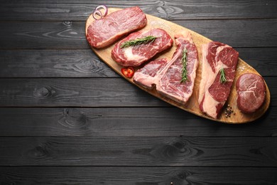 Pieces of raw beef meat and spices on black wooden table, top view. Space for text