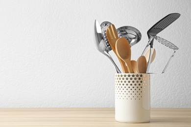 Photo of Set of kitchen utensils in stand on wooden table near light wall. Space for text