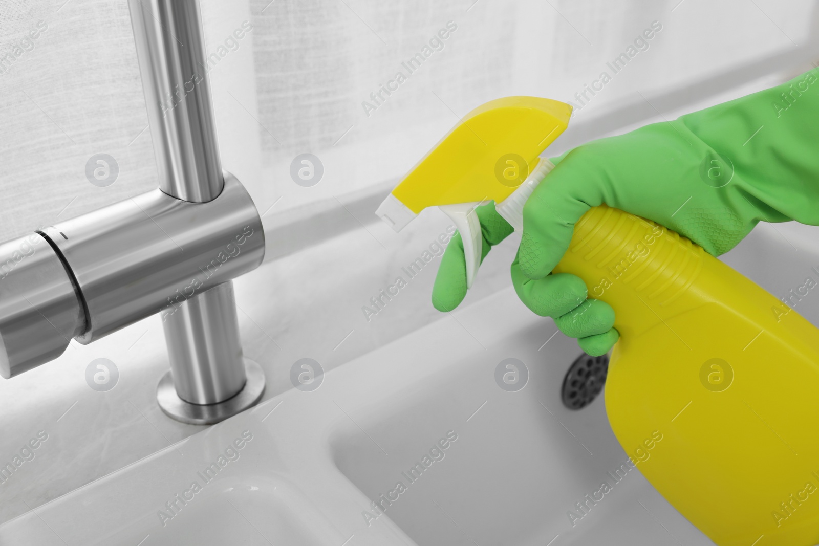 Photo of Woman with spray bottle near water tap in kitchen, closeup