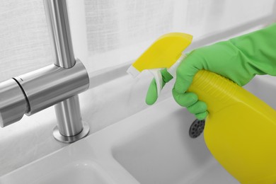 Photo of Woman with spray bottle near water tap in kitchen, closeup