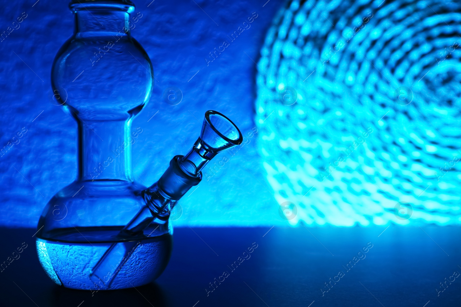 Photo of Closeup view of glass bong on table, space for text. Smoking device