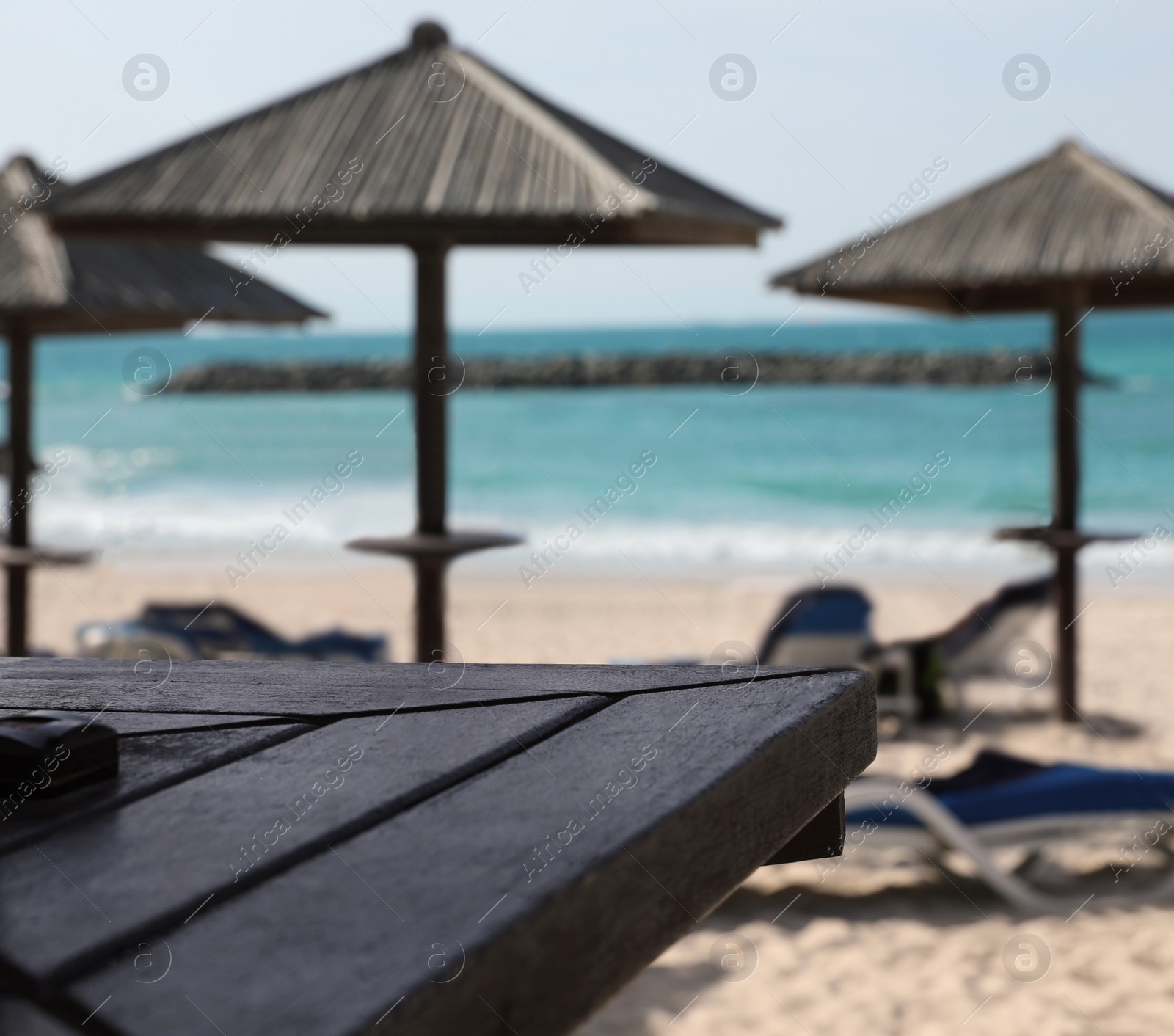 Photo of Wooden table and blurred view of tropical beach with umbrellas on background. Space for text