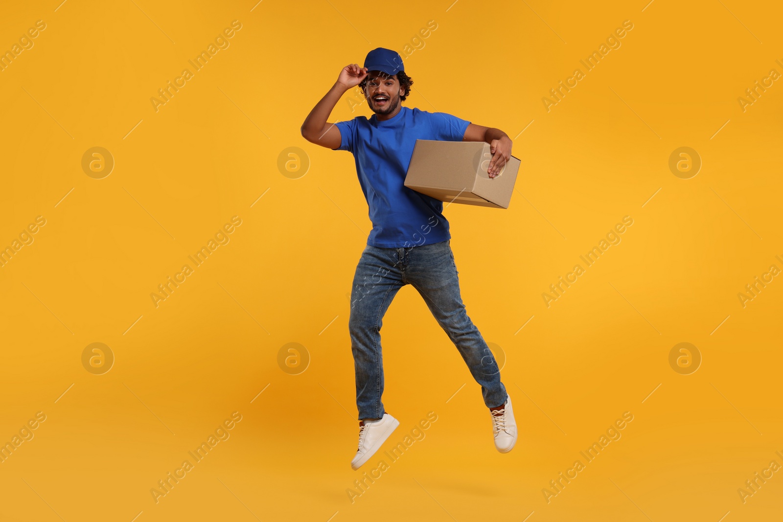 Photo of Happy courier with parcel jumping on orange background