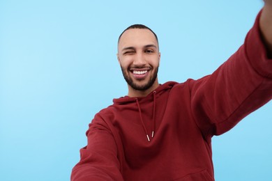 Smiling young man taking selfie on light blue background