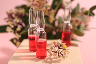 Photo of Stylish presentation of skincare ampoules and flowers on pink background, closeup