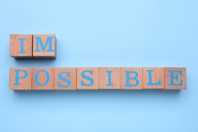 Photo of Motivation concept. Changing word from Impossible into Possible by removing wooden cubes on light blue background, flat lay