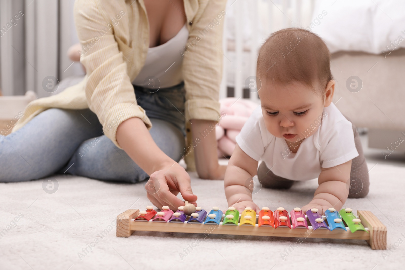 Photo of Cute baby and mother playing with xylophone on floor at home