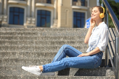 Photo of Young woman with headphones listening to music on stairs. Space for text