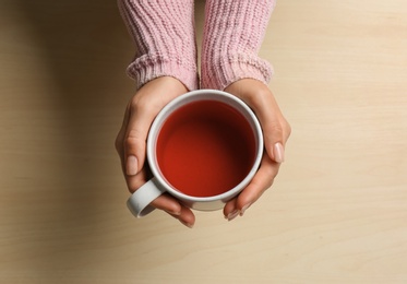 Photo of Woman holding cup of tea at wooden table, top view