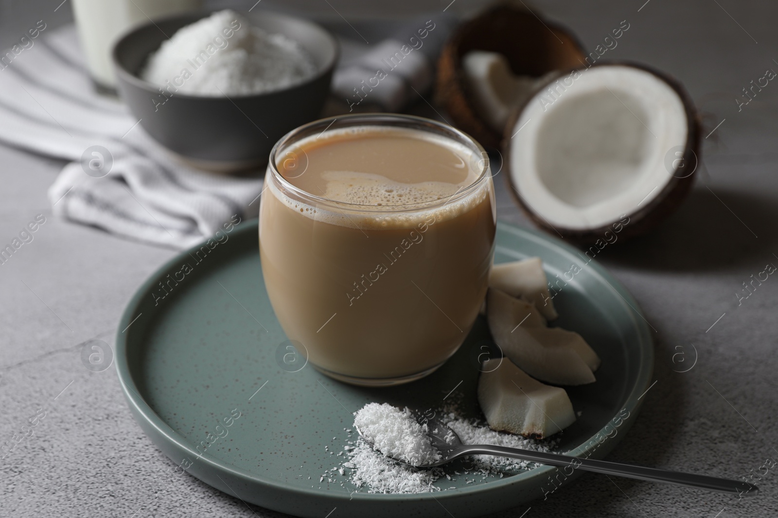 Photo of Glass of coffee with coconut milk, pieces and flakes on light grey table