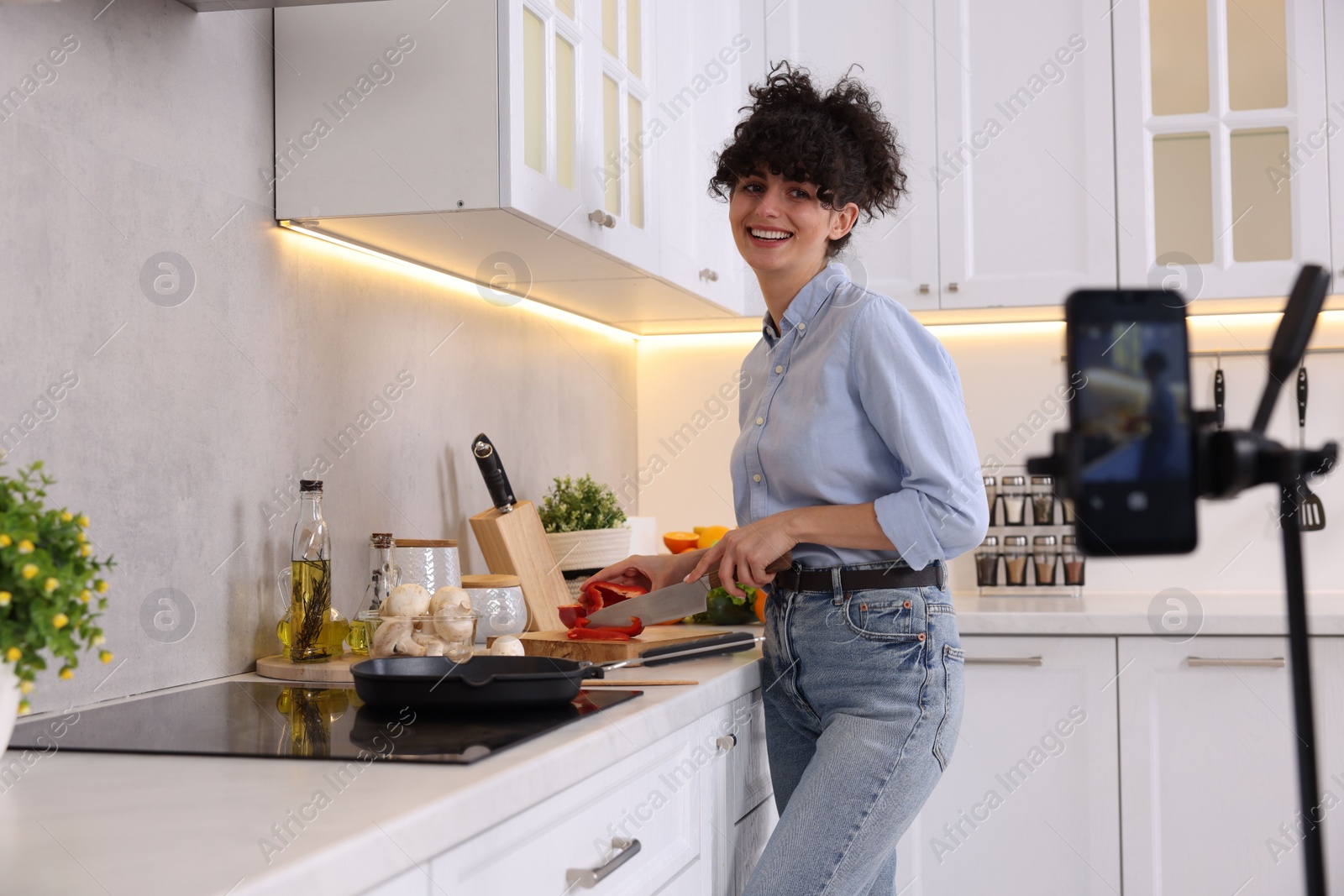 Photo of Smiling food blogger cooking while recording video in kitchen