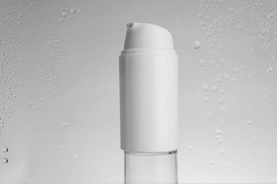 Bottle with moisturizing cream on grey background, view through wet glass