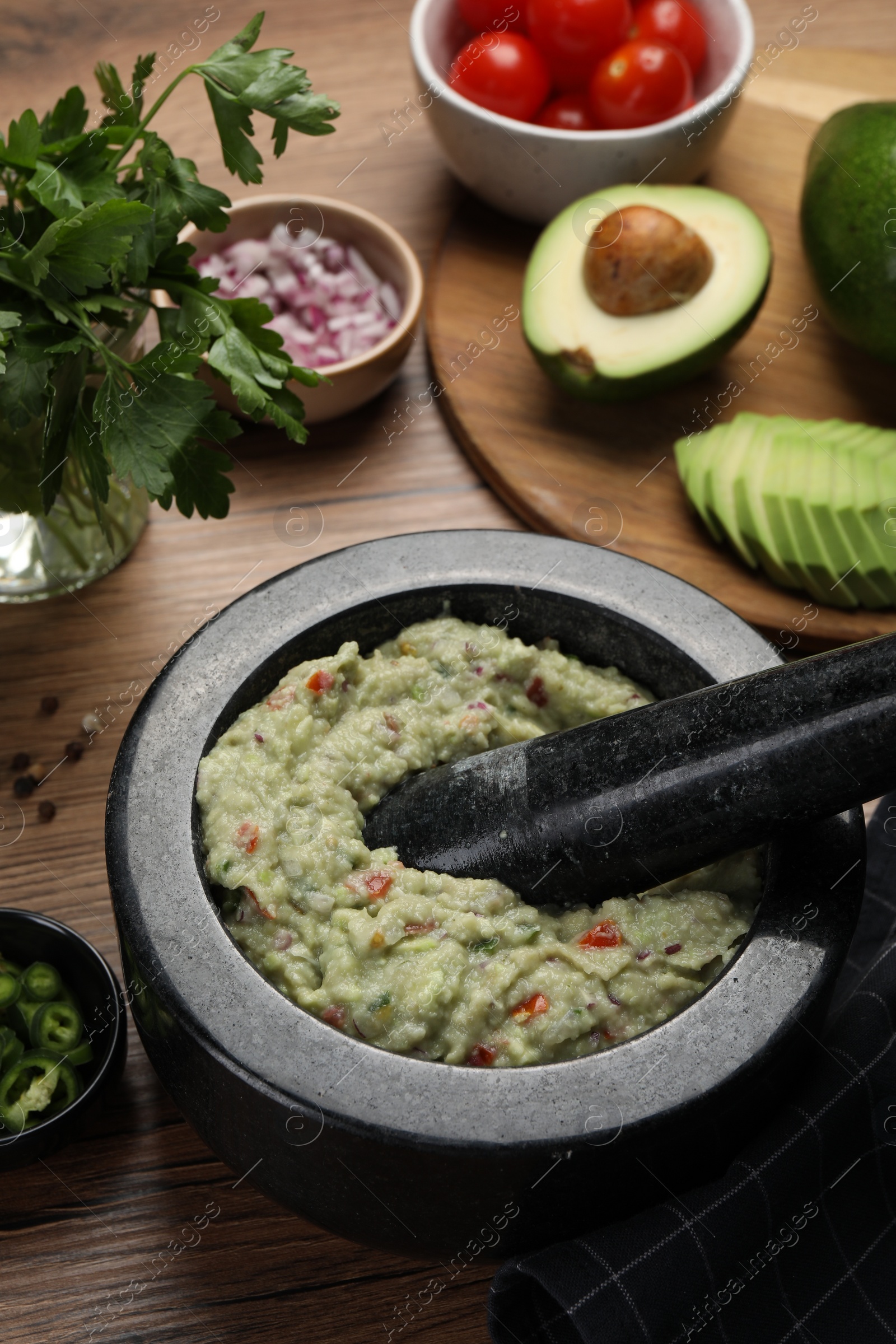 Photo of Delicious guacamole in mortar and ingredients on wooden table, closeup