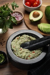 Delicious guacamole in mortar and ingredients on wooden table, closeup