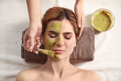 Cosmetologist applying mask onto woman's face in spa salon, top view