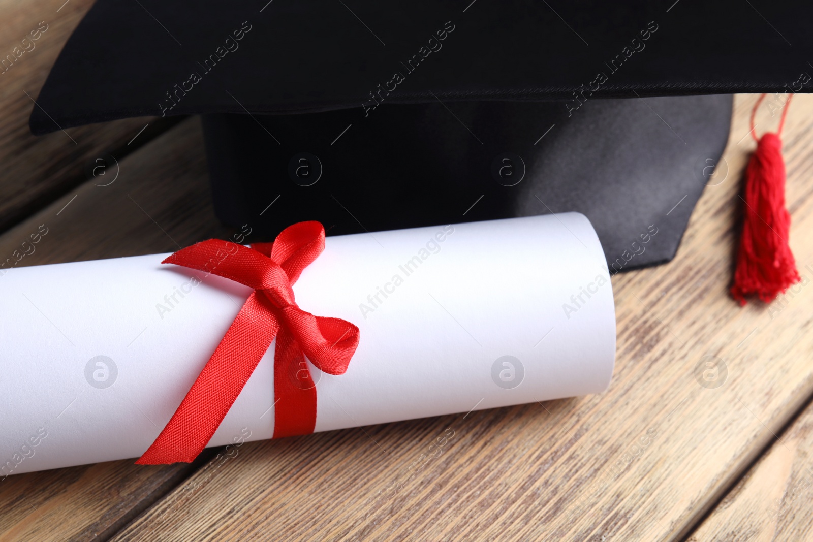 Photo of Graduation hat and student's diploma on wooden table, closeup