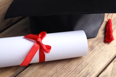 Graduation hat and student's diploma on wooden table, closeup