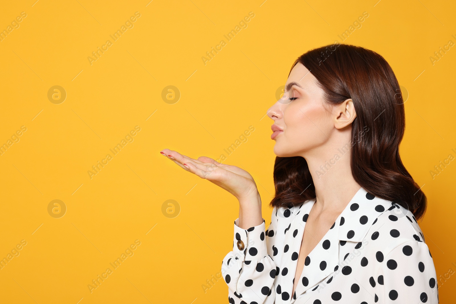 Photo of Beautiful young woman blowing kiss on yellow background. Space for text