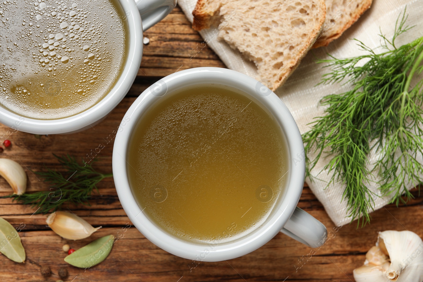 Photo of Hot delicious bouillon in cups on wooden table, flat lay