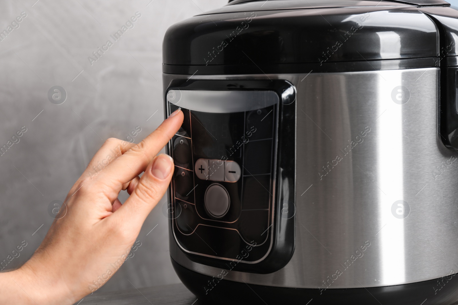 Photo of Woman turning on modern electric multi cooker on grey background, closeup