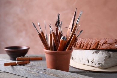 Photo of Clay and set of crafting tools on grey wooden table in workshop, closeup