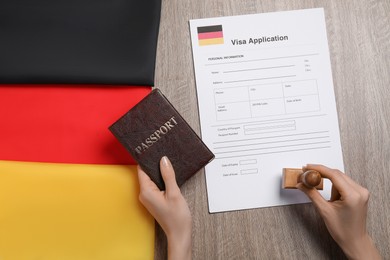 Photo of Immigration to Germany. Woman with passport stamping visa application form at wooden table, top view