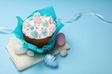 Photo of Traditional Easter cake with meringues and painted eggs on light blue background, space for text