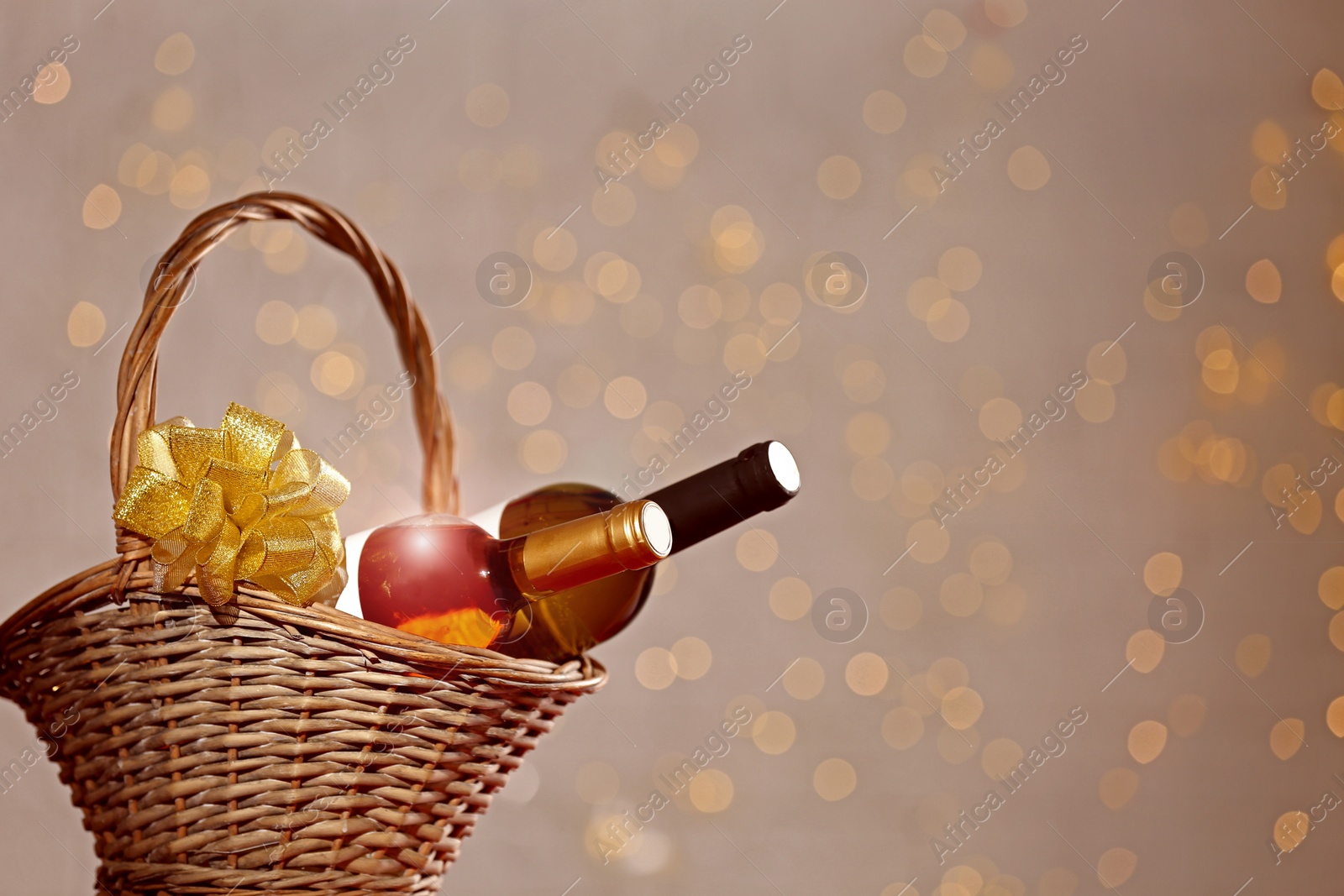 Photo of Bottles of wine in wicker basket with bow against blurred lights. Space for text